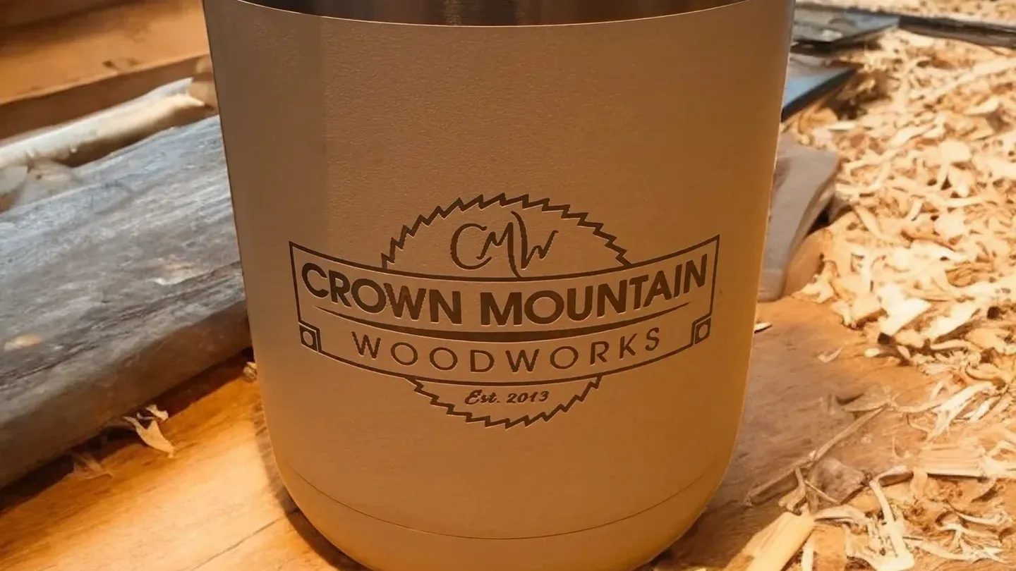 Engraved Crown Mountain Woodworks tumbler on a woodshop bench